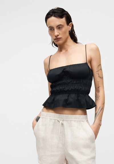 Μαύρο τοπ πεπλούμ με λεπτές τιράντες, κορσέ με πιέτες και φαρδιά τελείωμα. Συνδυάζεται με ανοιχτό μπεζ λινό παντελόνι, με πλαϊνές τσέπες.
