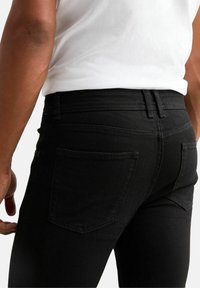 Svarta denimjeans med slim fit, synliga bakfickor och stickade detaljer. I kombination med en enfärgad vit skjorta.