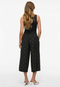 Melni rakstaini plati bikses ar brīvu griezumu, piedāvā ar auklu regulējamu jostu un sudraba dimanta formas rakstu visā virsmā. Valkā ar pieguļošu melnu topu.