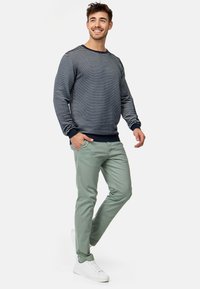 Marineblauw en wit gestreepte sweatshirt met omgeslagen mouwen, gecombineerd met lichtgroene slim fit chino's en witte sneakers, casual staand met handen in de zakken.