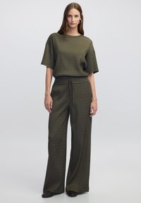 Oliwkowy sweter z krótkimi rękawami zestawiony z dopasowanymi spodniami o szerokich nogawkach z elastycznym pasem. Gładka faktura, casualowy design.