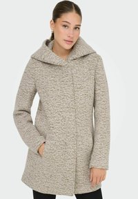 Manteau en mélange de laine beige clair avec une grande capuche, surface texturée, poches avant et coupe droite. Présenté sur un modèle sur fond blanc.