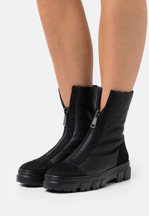 Zwarte enkellaarsjes van leer en suède, voorzien van twee zijritsen, een grove zool en een textuurachtig bovenwerk.