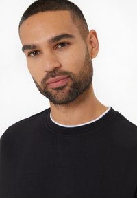 Czarna bluza z okrągłym dekoltem, teksturowana tkanina i subtelne detale szwów. Posiada białą lamówkę kołnierzyka wewnętrznego.