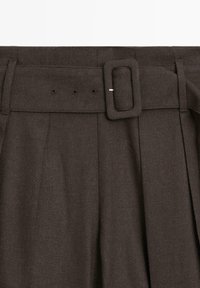 Donkerbruine plissébroek met een brede tailleband, voorzien van een rechthoekige gesp en meerdere riemgaatjes voor aanpassing.
