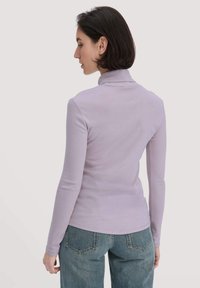 Hellblaues langärmliges Oberteil mit Stehkragen, aus weichem Stoff gefertigt. Kombiniert mit hochgeschnittenen blauen Jeans, die eine figurbetonte Silhouette zeigen.