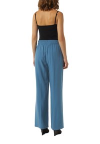 Spodnie z podwyższonym stanem, elastycznym pasem w niebieskim materiale. Szerokie nogawki i gładka tekstura. Połączone z czarną, dopasowaną bluzką.