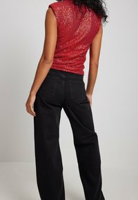 Haut sans manches rouge en tissu texturé, associé à un jean noir taille haute avec poches classiques et une coupe décontractée.