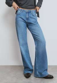 Jeans en denim bleu clair taille haute à jambes larges, dotés de poches avant, d'une fermeture à bouton et de coutures décoratives le long des coutures.