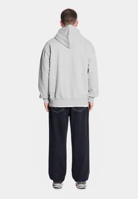 Szara bluza z kapturem o luźnym kroju i ściągaczami na rękawach, zestawiona z ciemnoniebieskimi workowatymi spodniami i trampkami, widok z tyłu.