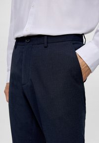Pantaloni navy realizzati in tessuto testurizzato con un design a gamba dritta. Presentano tasche laterali, passanti per cintura e una chiusura a bottone in vita.