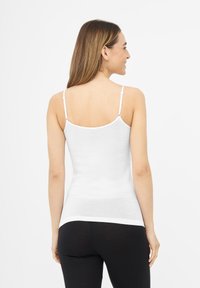 Camisole blanche à fines bretelles, coupe ajustée, texture douce et finition lisse. Portée avec des leggings noirs, vue de dos.