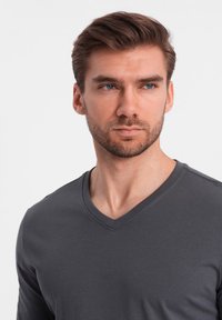 Graues Langarm-V-Ausschnitt-Shirt aus weichem Stoff, mit einem schlichten Design und glatter Textur, mit einer figurbetonten Silhouette und minimalen Akzenten.