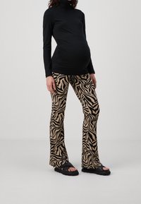 Svart långärmad topp i kombination med beiga zebramönstrade utsvängda byxor. Byxorna har ett texturerat mönster och kompletteras av svarta sandaler.