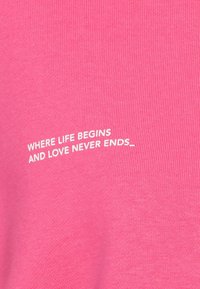 Camicetta rosa a maniche corte con texture a coste, con testo bianco che recita "DOVE INIZIA LA VITA E L'AMORE NON FINISCE MAI" disposto in un layout curvo.