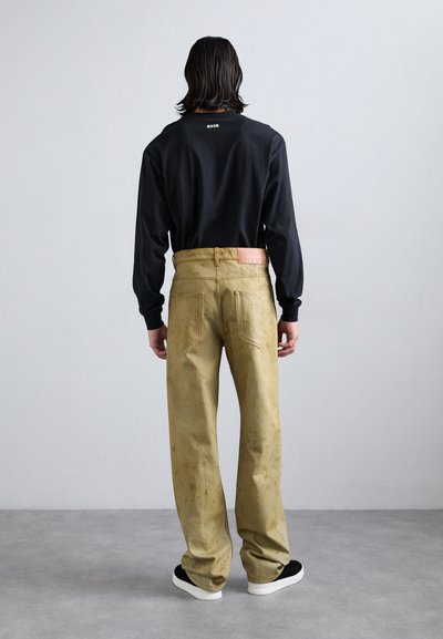 Maglietta nera a maniche lunghe e pantaloni larghi color khaki con una texture sbiadita, dotati di una patch di pelle sul retro, indossati con sneakers nere.