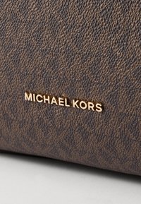 Materiale marrone testurizzato con un motivo geometrico; presenta un logo dorato "MICHAEL KORS" ben in vista sulla superficie.