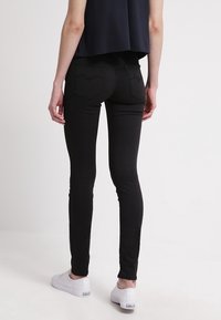 Jeans skinny negros con una textura suave, con bolsillos traseros y detalles de costura sutiles, combinados con zapatillas blancas.