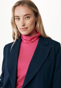 Námořnický blejzr přes růžový rolák, předvádějící hladkou tkaninu, střih na míru a kontrastní barvy. Čisté linie a žádné viditelné vzory.