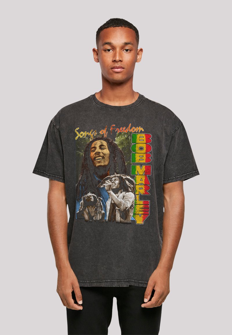 Schwarzes Grafik-T-Shirt mit dem Aufdruck "Songs of Freedom" und visuellen Darstellungen von Bob Marley, darunter farbenfroher Text und detaillierte Bilder von Marley und Musikern.