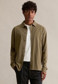 Olijfgroene, lange mouwen, knoopsluiting overhemd van zachte stof, met een kraag, frontale knoopsluiting en subtiele naaddetails. Gedragen over een wit shirt.