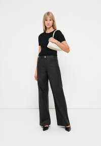 Un tricou negru mulat, asortat cu o pereche de pantaloni negri, cu talie înaltă și laturi largi. Modelul ține o geantă mică de culoare crem. Pantofii sunt negri, cu un detaliu în formă de fundiță.