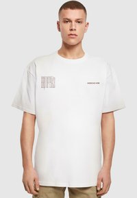 White short-sleeve t-shirt featuring printed text, round neckline, and a relaxed fit. Material appears soft with a smooth texture.