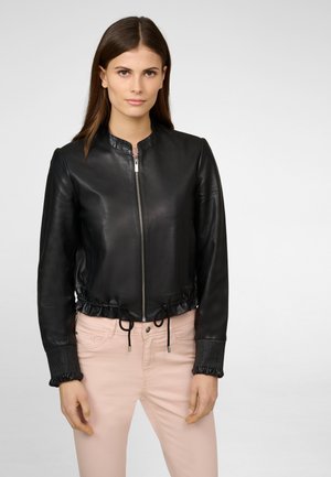Giacca di pelle nera con colletto rotondo, zip frontale, vita cintrata e polsini a coste. Abbinata a jeans rosa chiaro.
