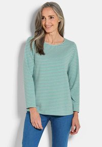 Lichtgroene langemouwen shirt met horizontale witte strepen. Zachte stof, ronde hals en een relaxed fit. Gecombineerd met blauwe jeans.
