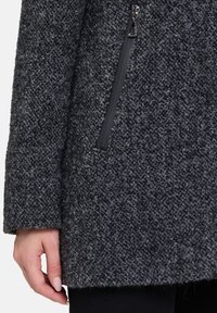 Płaszcz z mieszanki wełny w ciemnoszarym kolorze z teksturowaną powierzchnią. Posiada zasuwaną kieszeń po lewej stronie oraz rękawy o średniej długości.