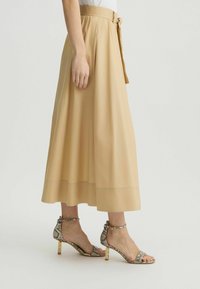 Gonna midi beige con vita arricciata e dettaglio con fiocco, abbinata a sandali con tacco a strisce a stampa serpente con dettagli metallici.