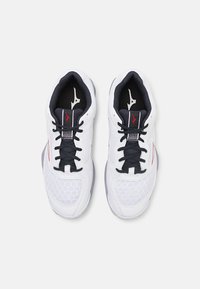 White athletic shoes with black laces, mesh detailing, and red accents. Features a textured midsole and a sleek, rounded design.