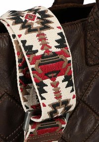 Sac en cuir marron avec une sangle à motifs présentant des designs géométriques rouges, noirs et beiges, maintenu par un clip en métal argenté.