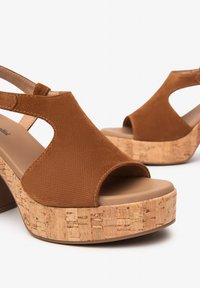 Chaussures à plateforme ouvertes brunes avec une tige texturée et un talon en liège. Caractéristiques : une bride de cheville et une semelle lisse beige.