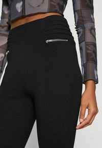Zwarte high-waisted legging met ribbeldetails in de tailleband en ritszakken op de heupen. Glad materiaal met een getailleerd silhouet.