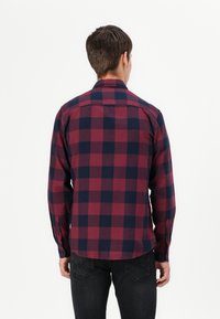 Camicia a quadri rossa e blu navy con bottoni, maniche lunghe e orlo arrotondato, realizzata in tessuto strutturato. Presenta polsini con bottoni e un colletto classico.