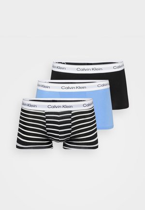 Kolme paria miesten bokserihousuja: yksi musta, yksi tasaisesti vaaleansininen ja yksi musta-valkoraidallinen, kaikissa valkoinen "Calvin Klein"-vyötärönauha.