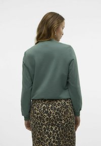 Sweatshirt vert avec des manches longues, un col rond et une texture lisse. Associé à une jupe à imprimé léopard avec des poches visibles.