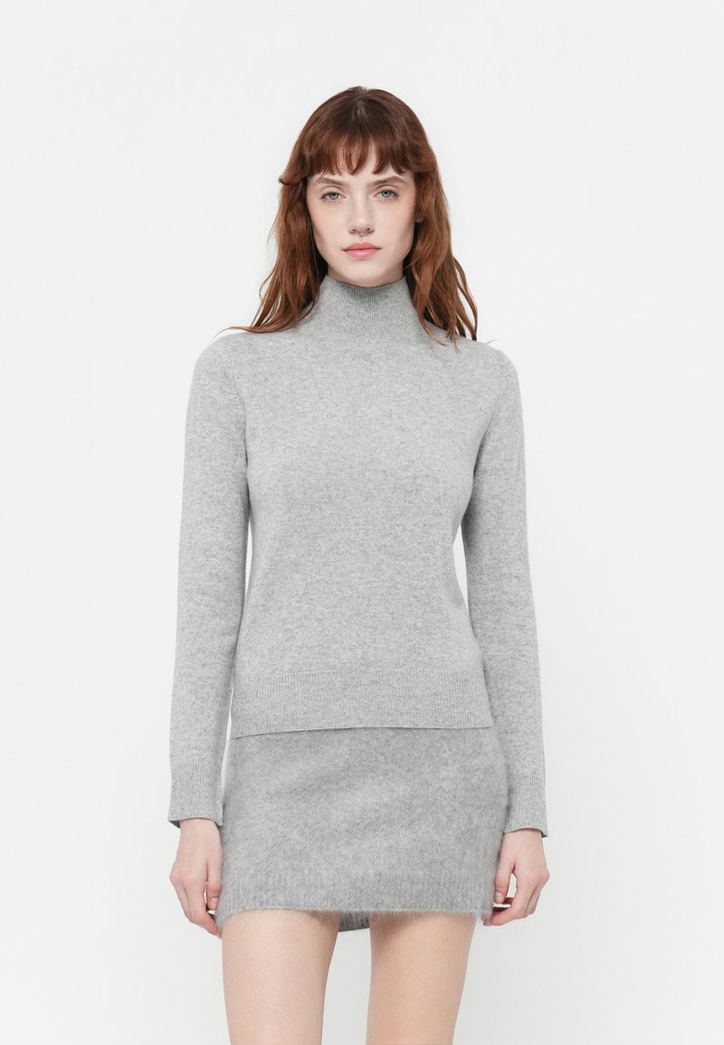 Pelēks adīts turtlenecks džemperis ar garajām piedurknēm, mīksta tekstūra un pieguļošs dizains, kombinēts ar atbilstošu pelēku mini svārku.