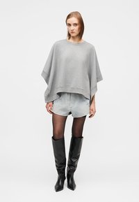 Svetlosiv ohlapen pulover velike velikosti, kratke jeans hlače in črni usnjeni škornji do kolen. Gladek tekstura in minimalističen dizajn.