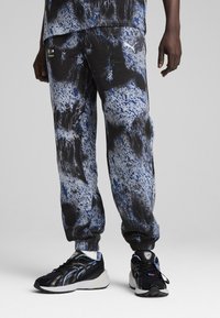 Sorte joggers med blå og grå abstrakt mønster, elastiske manchetter og logo på den bageste lomme. Kombineret med sorte sneakers med blå accenter.