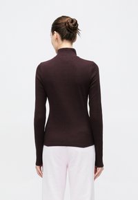 Brązowa prążkowana bluzka z długim rękawem i wysokim kołnierzem. Charakteryzuje się dopasowanym krojem i gładką teksturą, zestawiona z jasnoróżowymi spodniami.