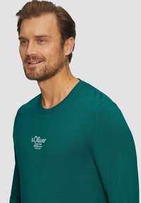Türkise langärmlige T-Shirt mit Rundhalsausschnitt. Mit dem s.Oliver-Logo in Weiß auf der Brust bestickt. Weiches Baumwollmaterial.