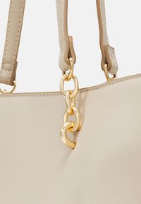 Sac à main beige avec des anses cousues attachées par de grands maillons de chaîne dorés brillants sur une surface en cuir lisse.