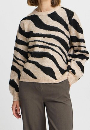 Pull en maille beige avec de larges rayures zebra noires. Il présente un col rond, de longues manches bouffantes et un ourlet côtelé. Texture douce.