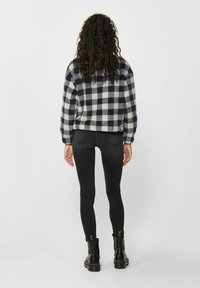 Veste en polaire à carreaux bleu marine et crème, coupe courte avec épaules tombantes. Jeans noirs slim et bottines noires avec accents dorés.