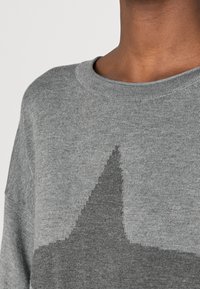 Pull en maille grise avec un col rond, présentant un motif géométrique en gris plus foncé, texture douce et coupe ample.