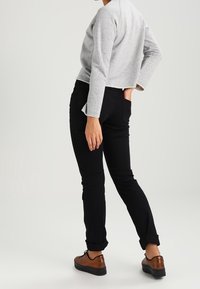 Jersey gris corto, jeans negros ajustados y zapatos marrones. Jeans arremangados en los tobillos, textura suave del jersey, diseño simple.