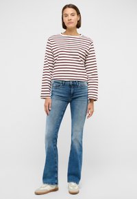Striped long-sleeve shirt in cream with burgundy stripes, paired with faded blue flared jeans and light-colored sneakers. Smooth fabric and casual fit.