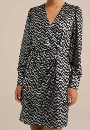 Vestido de patrón zigzag en blanco y negro con escote en V, mangas largas y cintura ajustada, hecho de una tela ligera y semitranslúcida.
